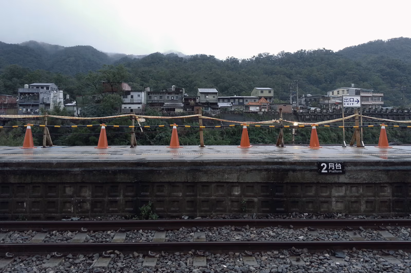 A photograph of a railway bridge in Keelung, Taiwan, with orange cones and a construction site in the background.